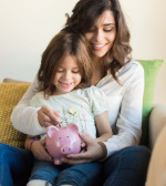 mom and daughter putting money in piggy bank