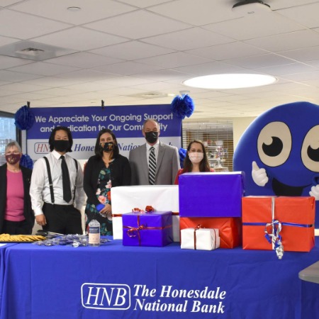 five employees from the Bank and mascot behind a table at the hospital